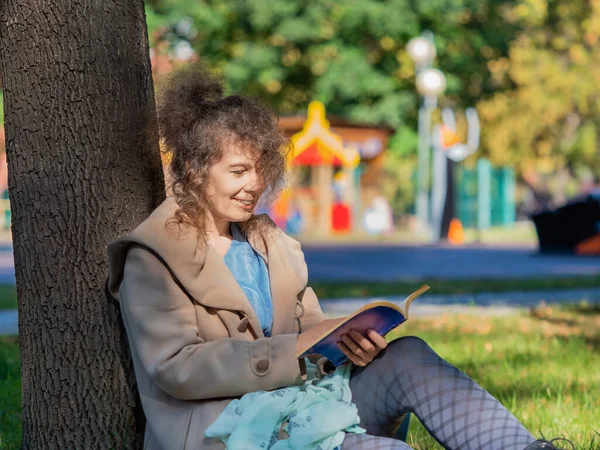 Kobieta w średnim wieku z książką w parku. Siedzi na trawie i czyta książki. Pojęcie odpoczynku od gadżetów, smartfonów i Internetu. — Zdjęcie stockowe