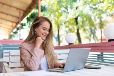 Yazlık kafede dizüstü bilgisayar başında çalışan bir kadın. Dizüstü bilgisayara bakıyor ve gülümsüyor..