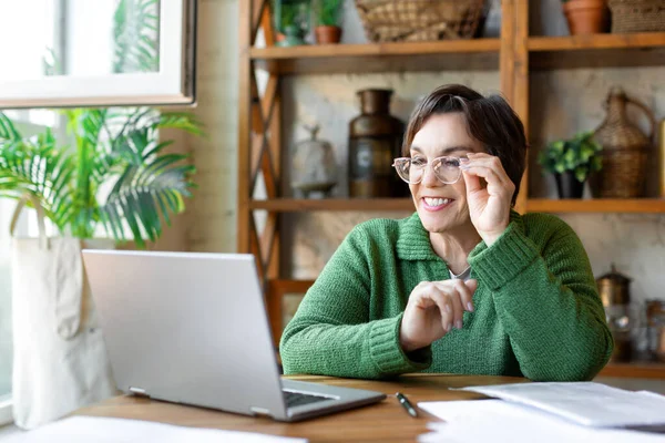 日常生活の中で現代的な技術の概念-オンラインビデオ通話中にラップトップモニターの前で笑顔のシニア女性. — ストック写真