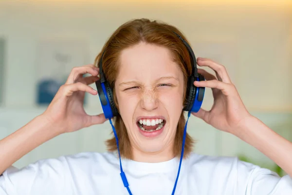 Adolescente pelirroja con auriculares azules. Escucha música terrible y no le gusta.. — Foto de Stock
