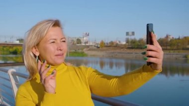 Orta yaşlı bir kadın çevrimiçi video görüşmesi yapıyor. Sokakta akıllı telefonuyla video görüşmesiyle konuşuyor..