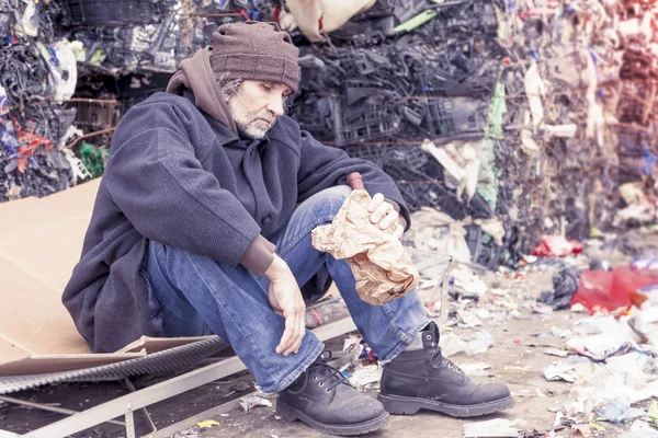 Homeless man with a bottle of red wine in landfill — Stock Photo, Image