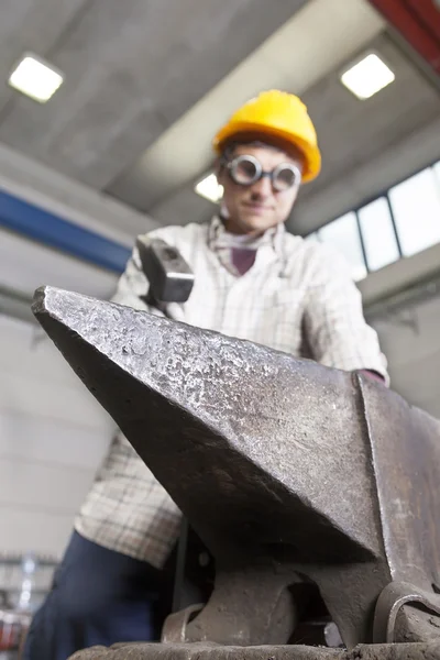 Metalúrgico trabalha metal com martelo na bigorna — Fotografia de Stock