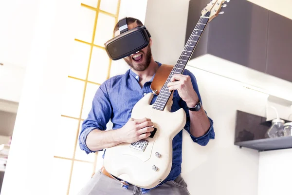 Adulto joven tocando la guitarra en casa usando el visor para re aumentada — Foto de Stock