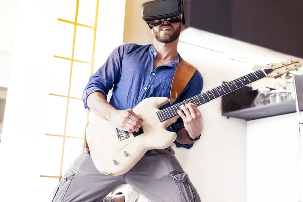 Adulto joven tocando la guitarra en casa usando el visor para re aumentada — Foto de Stock