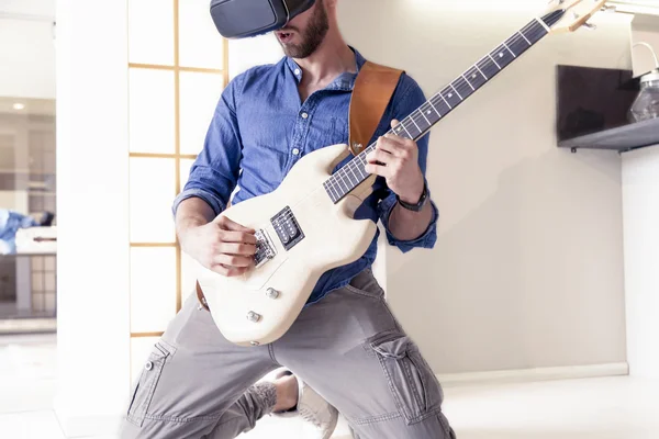 Adulto joven tocando la guitarra en casa usando el visor para re aumentada — Foto de Stock