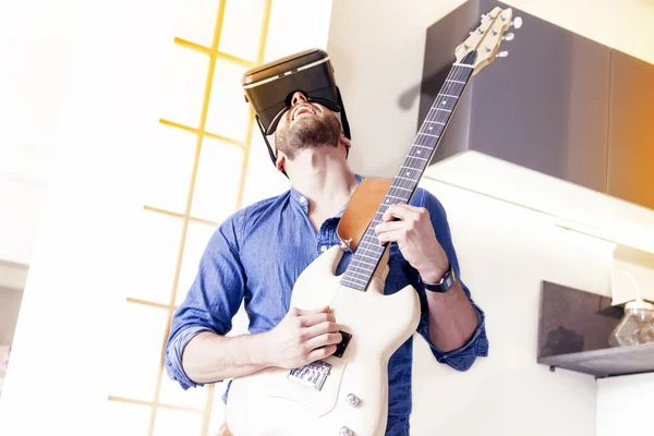 Молодой человек играет на гитаре дома с помощью зрителя для увеличения ре — стоковое фото