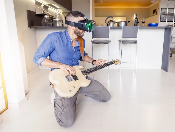 Adulto joven tocando la guitarra en casa usando el visor para virtual real — Foto de Stock