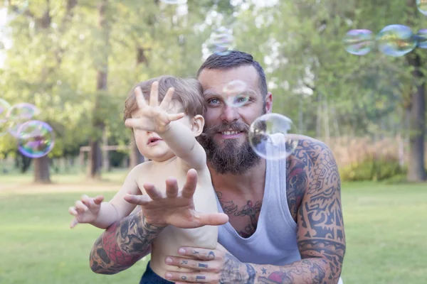 Niño se divierte con su padre y trata de tomar burbujas de jabón — Foto de Stock