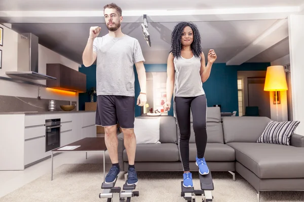 Jovem casal ele treina com a máquina passo em casa — Fotografia de Stock