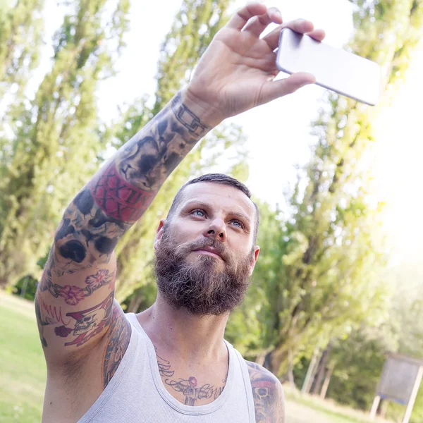 Wytatuowany Brodaty mężczyzna bierze sobie selfie w parku — Zdjęcie stockowe