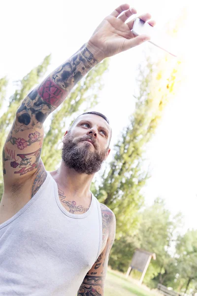 tattooed bearded man takes a selfie in the park