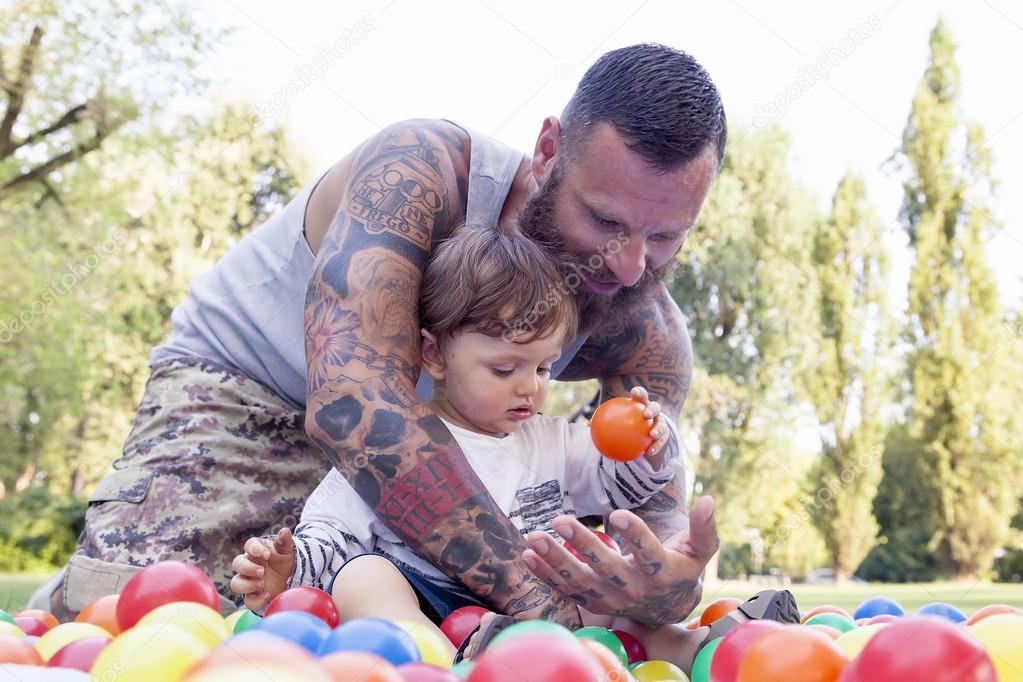 tattooed father have fun with his son in the park with colored b