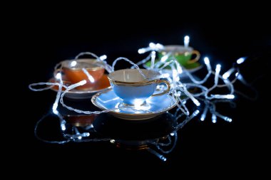 Siyah arka planda renkli bardakların üzerine çizgili Noel ışıkları. Noel ruhu konsepti