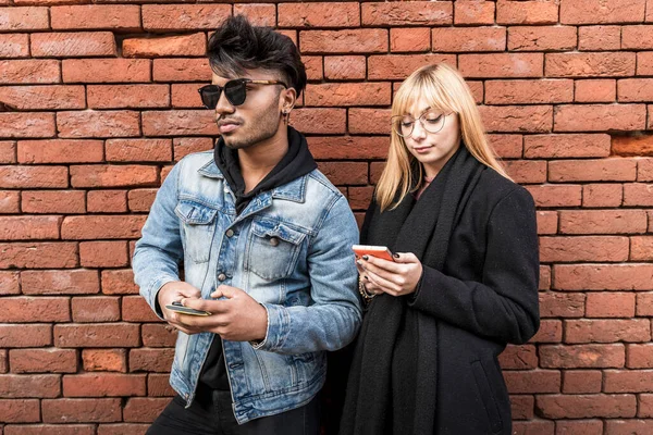 young multi-ethnic couple in front of brick wall using smartphone to share content on social networks