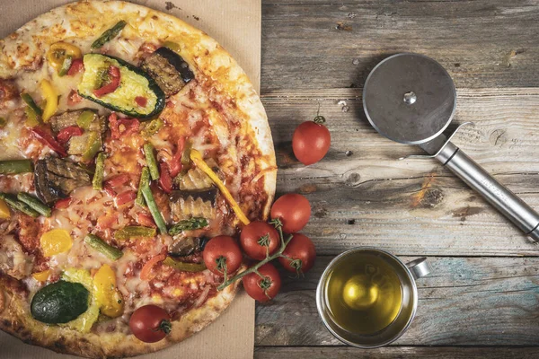 Tasty grilled vegetable pizza cooked with ingredients on wooden background. Top view