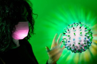 Covid-19 molekül sembolünün önündeki yüz maskeli kadın.