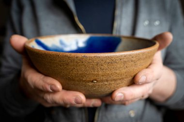 Bir çömlekçinin elleri içinde mavi boyalı bir kase gösteriyor.