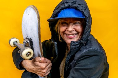 Funny portrait of mature woman. Lady having fun with skate dressed as rapper. Mature woman on colored backgrounds  clipart