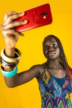 Geleneksel elbiseli genç Afrikalı kadın selfie çekiyor. Sarı arkaplanda stüdyo çekimi 