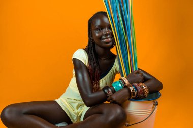Gülümseyen genç Afrikalı kız uzun renkli pipetlerle oynuyor. Sarı arkaplanda stüdyo çekimi 