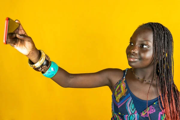 伝統的なドレスを着た若いアフリカ人女性が自撮りをします 黄色の背景で撮影したスタジオ — ストック写真