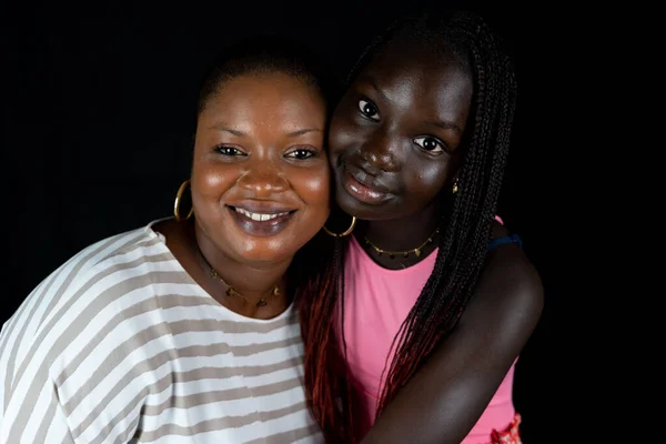 非裔美国人的母亲和女儿在黑人背景上欢快地拥抱在一起 — 图库照片