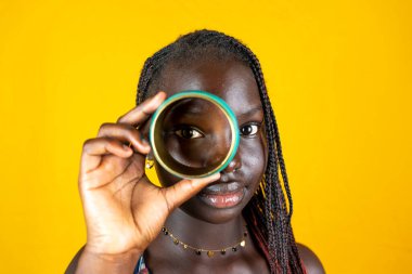 Etnik bir bileziğe bakarak eğlenen genç Afrikalı bir kızın portresi. Sarı arkaplanda stüdyo çekimi