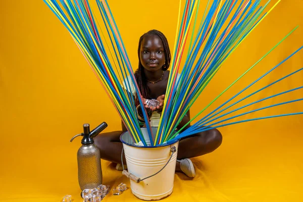 年轻可爱的非洲少年坐在那里准备一个巨大的鸡尾酒与冰和长长的五颜六色的饮水稻草 黄底工作室拍摄 — 图库照片