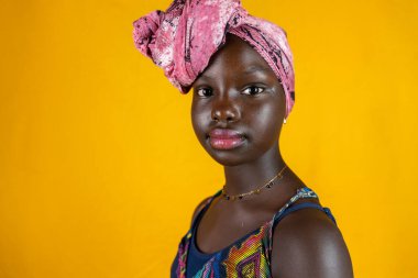 Sarı arka planda izole edilmiş kafasında renkli etnik eşarp olan Afrikalı kadın portresi