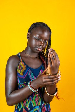 Geleneksel elbise ve bilezik takan Afrikalı genç bir kızın portresi. Sarı arkaplanda stüdyo çekimi