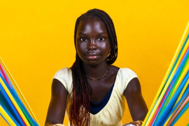 Oldukça genç Afrikalı bir genç uzun renkli pipetlerle oynuyor. Sarı arkaplanda stüdyo çekimi 