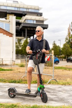 Banliyö hipster 'ı şehrin varoşlarında elektrikli scooter kullanıyor. Çevre taşımacılığı kavramı