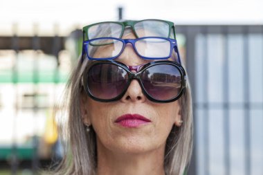 Bir sürü gözlük takan, ciddi yüzlü, olgun bir kadının komik portresi.