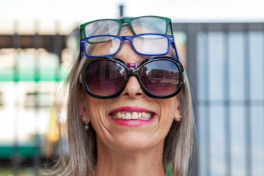 Bir sürü gözlük takan olgun bir kadının gülümsemesi ve komik portresi.