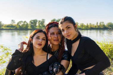 Üç kadının ailesi ve nehir kenarında poz veren bir köpek.