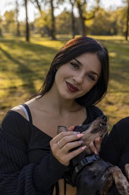 Gülümseyen, vakit geçiren ve sonbahar parkında köpeğine sevgi gösteren genç bir kadın.