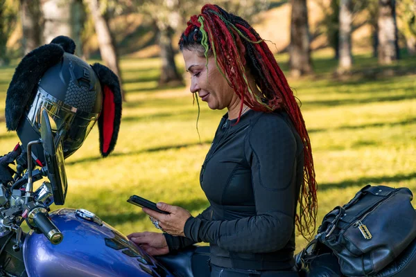 Motosikletli ve akıllı telefon kullanan renkli saçlı bir motorcu kadın.