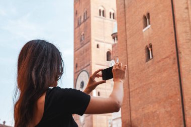 Akıllı telefon tutan, antik tuğla kulesinin seyahat fotoğraflarını çeken bir kadın.