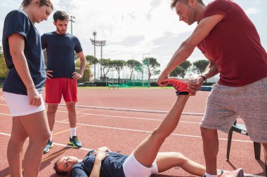 Spor koçu koşu pistinde yaralanan bir bayan sporcuya yardım ediyor.