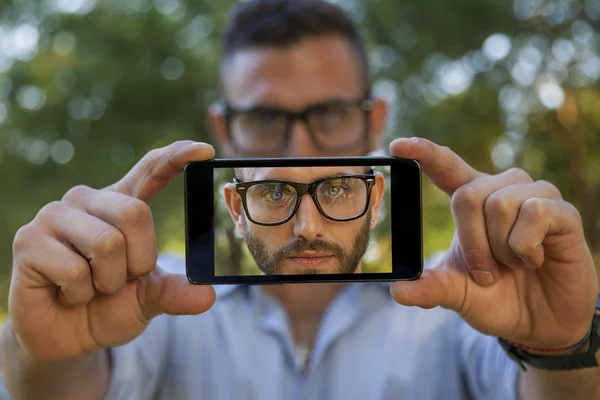 ハンサムな若い男は、スマート フォンと selfie を取る — ストック写真