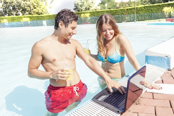 Bonita pareja joven con ordenador portátil en la piscina — Foto de Stock