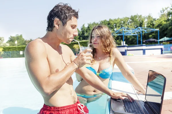 Bonita pareja joven con ordenador portátil en la piscina — Foto de Stock