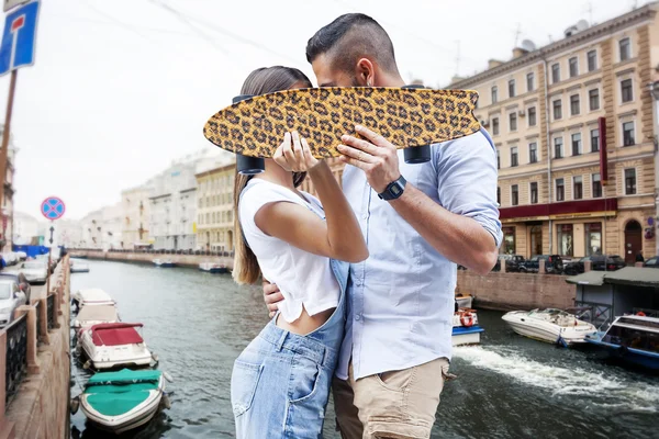 Junges Paar küsst sich hinter einem Skateboard — Stockfoto