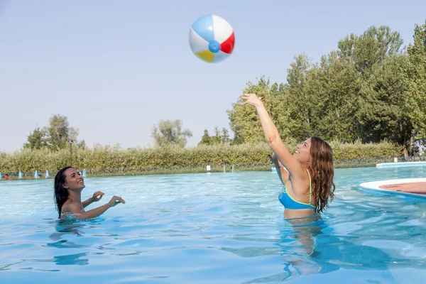 Feliz pareja de chicas relajándose en la piscina jugando con una pelota — Foto de Stock