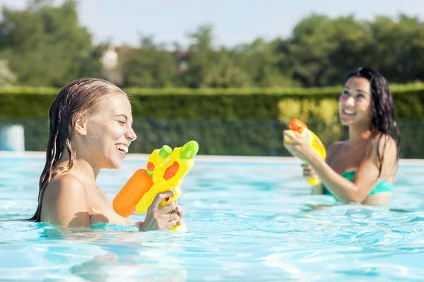 Chicas bonitas jugando con pistolas de agua en la piscina — Foto de Stock