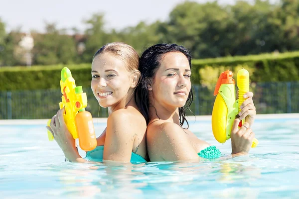 Chicas bonitas jugando con pistolas de agua en la piscina — Foto de Stock