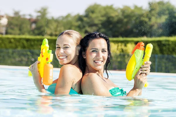 Chicas bonitas jugando con pistolas de agua en la piscina — Foto de Stock