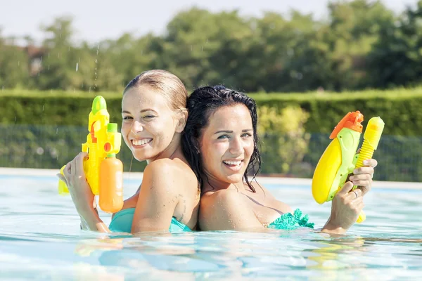Chicas bonitas jugando con pistolas de agua en la piscina — Foto de Stock