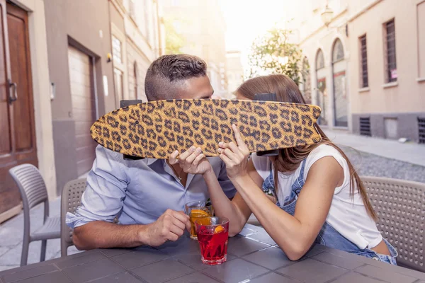 Young couple kissing hiding behind a skateboard in a downtown ba — Stock Photo, Image